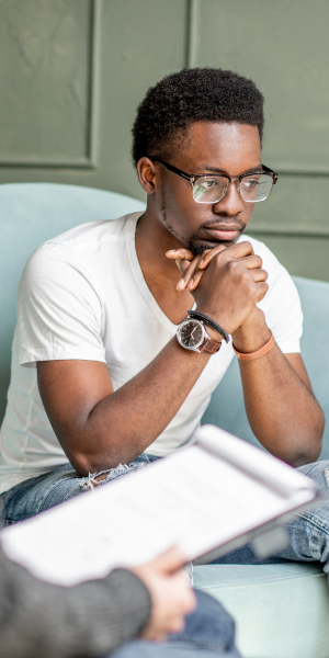 Young black man with his hands folded beneath his chin, listening to his therapist