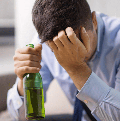 Man in distress with his head down and holding an alcoholic beverage portraying need for emergency addiction rehab